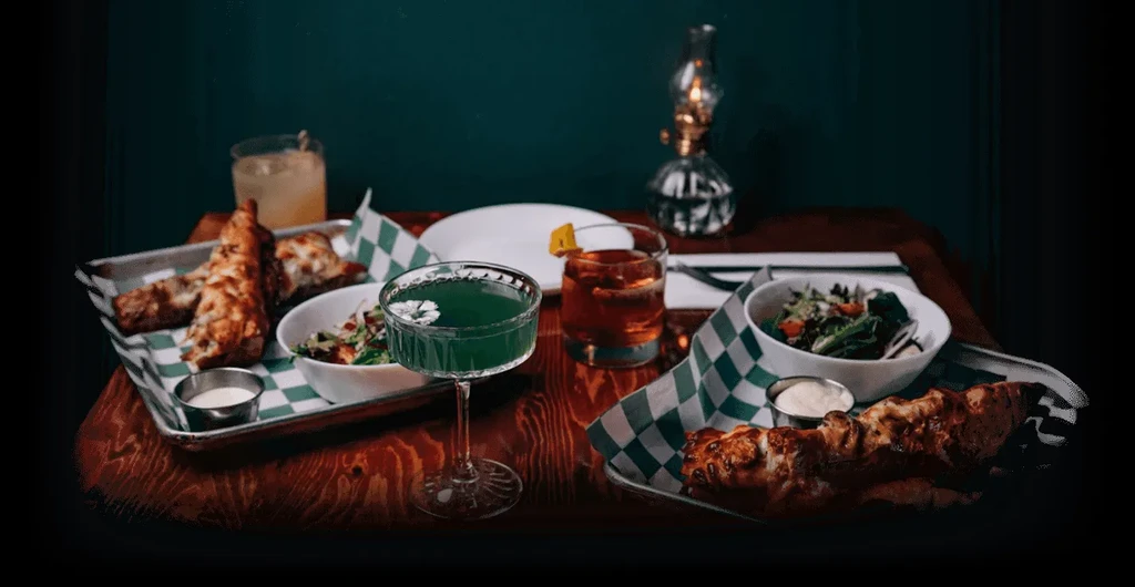Dimly lit wooden table with appetizers and garnished cocktails.