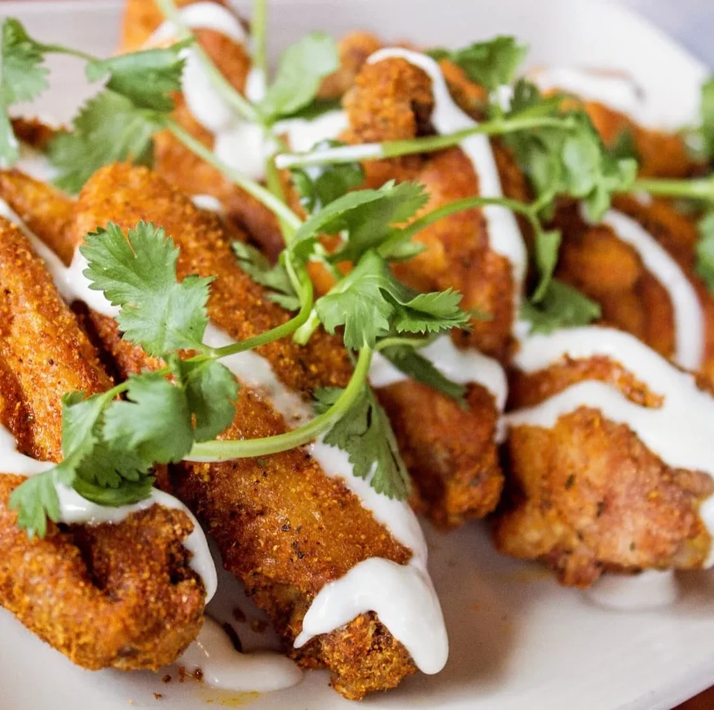 Golden-brown crispy fried chicken pieces drizzled with white sauce and cilantro.