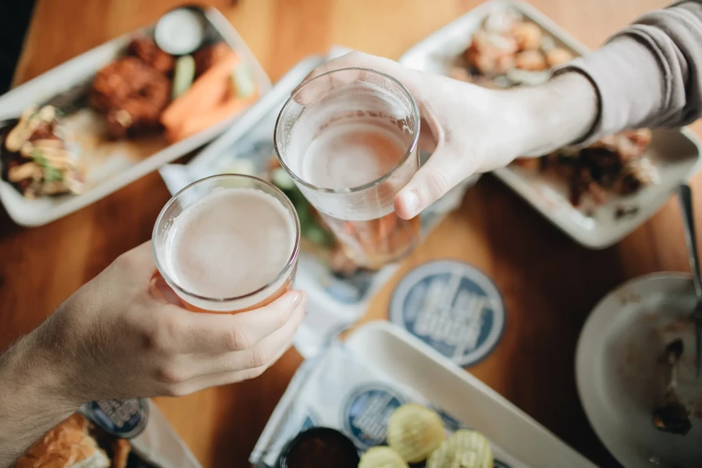 Two hands clinking golden beer glasses over blurred food.