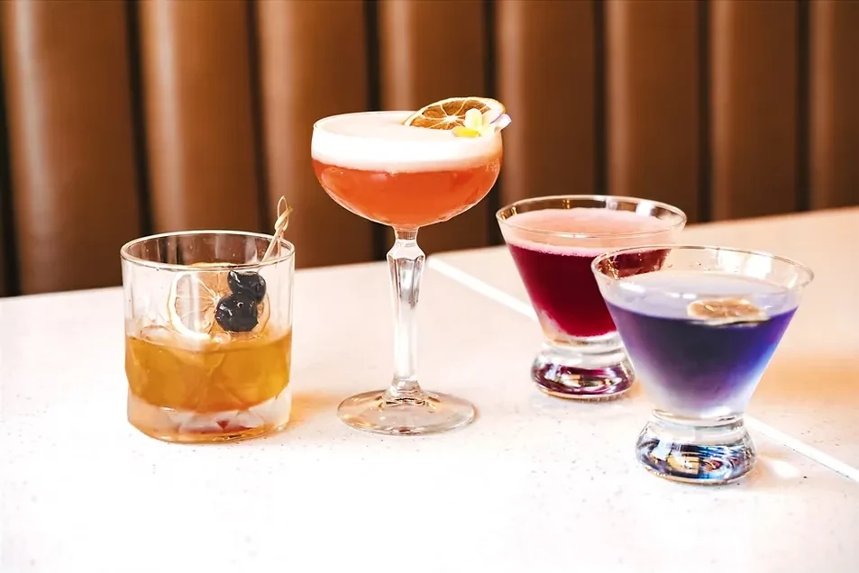Four distinct, colorful cocktails in various glasses on a white table.
