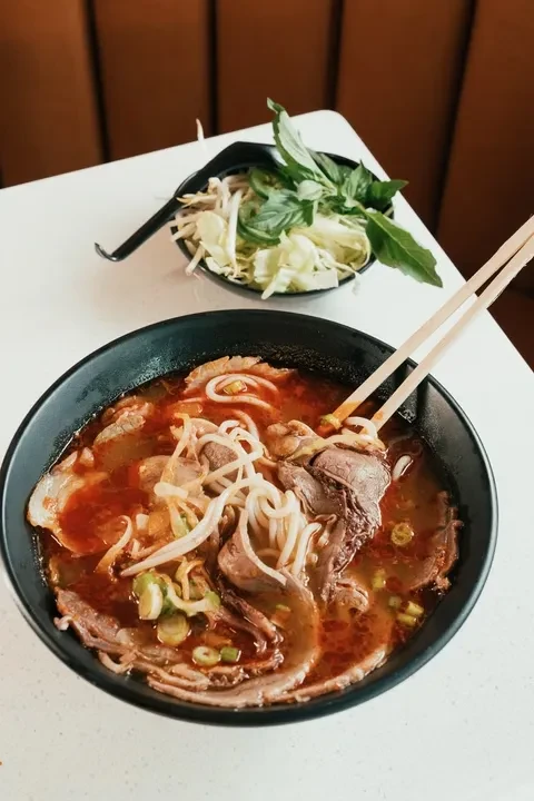 Vibrant Vietnamese beef noodle soup in black bowl with chopsticks.