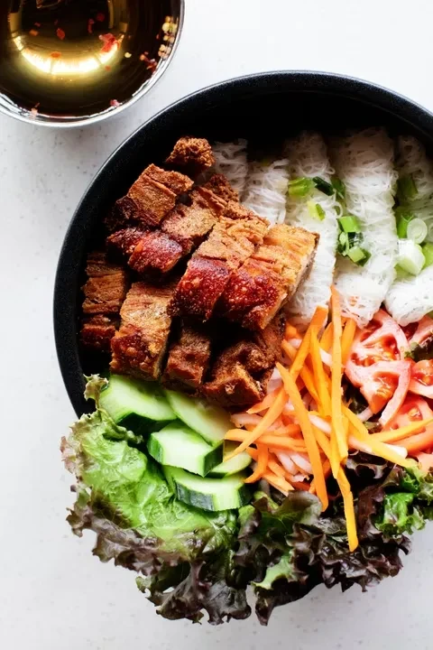 Black bowl of Vietnamese noodle salad with crispy pork belly.
