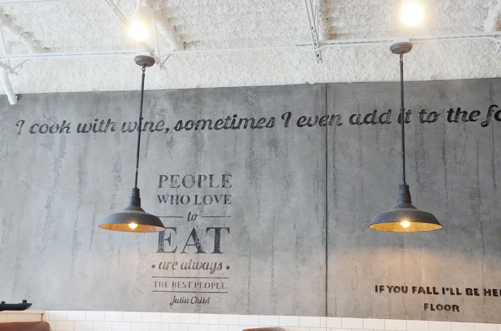 Textured gray restaurant wall with food quotes and industrial lights.