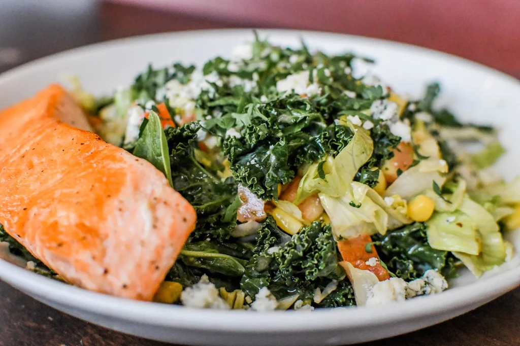 Salmon fillet and vibrant green kale salad with crumbled cheese.