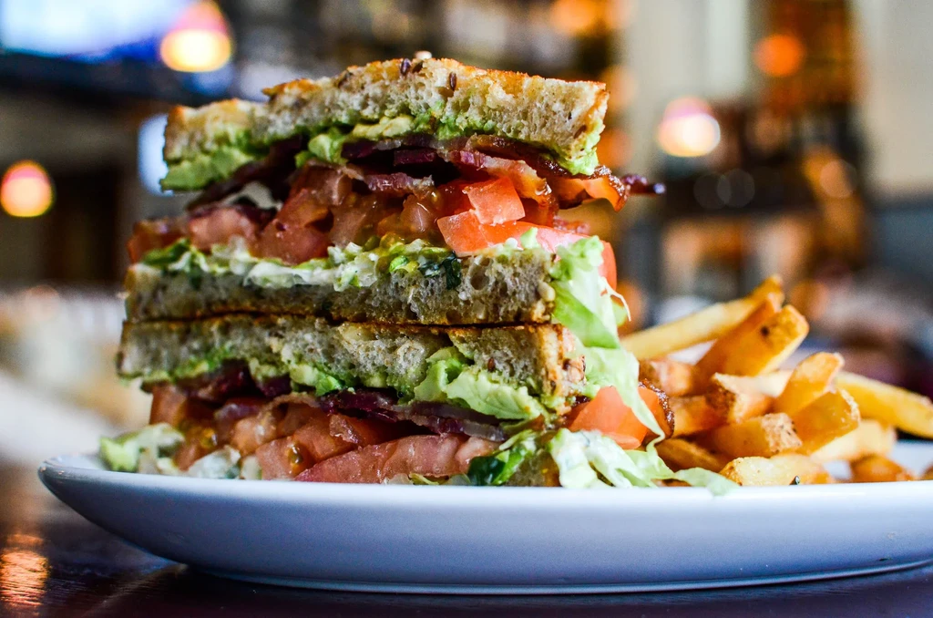 Multi-layered sandwich with avocado, bacon, tomato, lettuce, and fries.