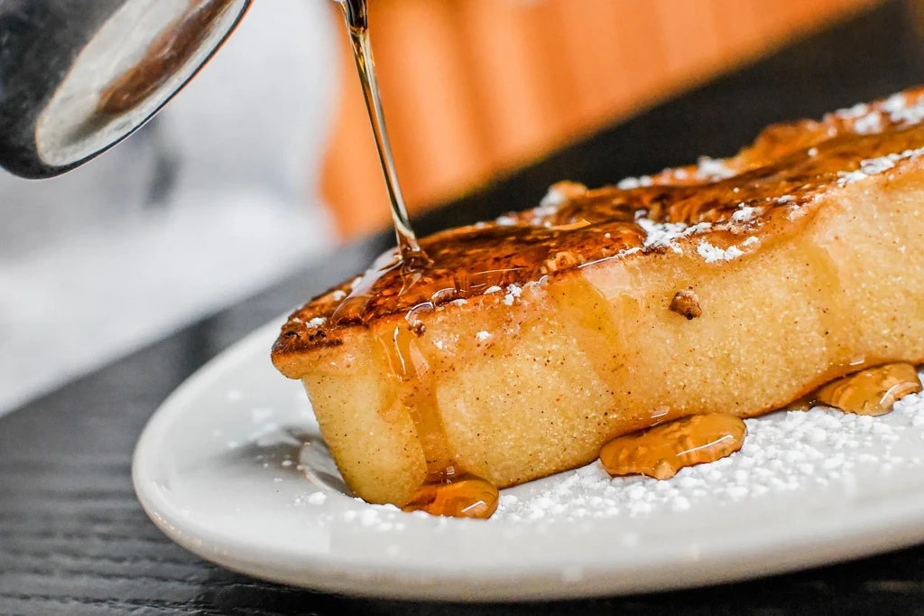 French toast with syrup pouring from a spoon, dusted with powdered sugar.