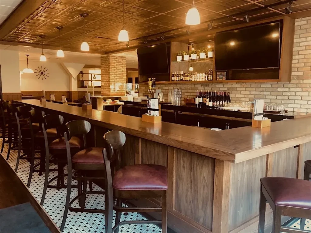 Empty L-shaped wooden bar, mosaic floor, brick walls, copper ceiling.