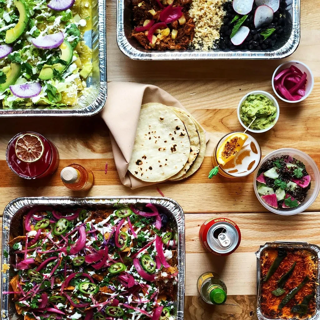 Overhead: Mexican catering dishes, drinks on a wooden table.