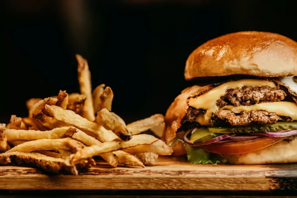 Double cheeseburger with vegetables and french fries on a wooden board.