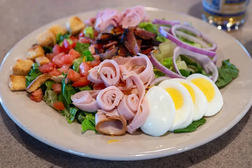 Vibrant salad with lettuce, tomatoes, deli meat, eggs, bacon, croutons.