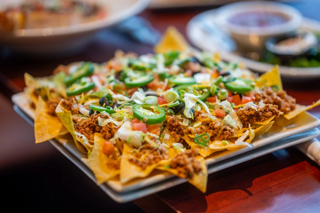Close-up of loaded nachos with meat, melted cheese, and fresh vegetables.