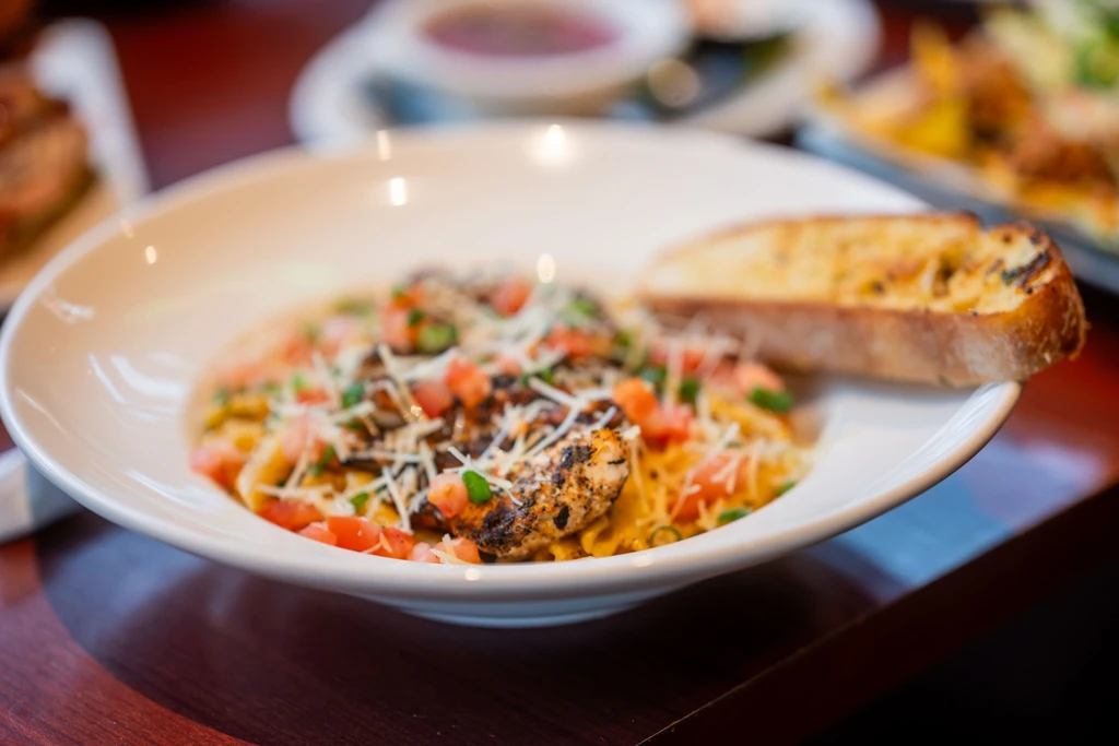 Grilled chicken pasta with cheese, tomatoes, green onions, and garlic bread.
