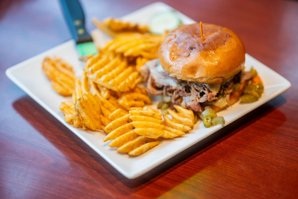 Hearty sandwich, waffle fries, and pickled vegetables on a white plate.