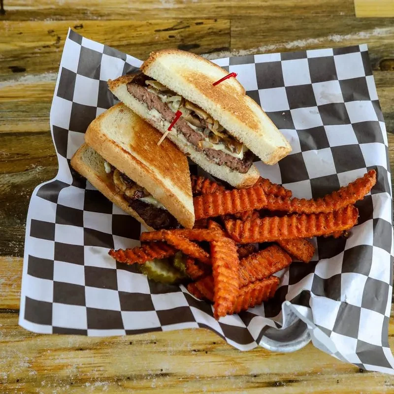 Grilled sandwich, sweet potato fries in checkered paper-lined basket.