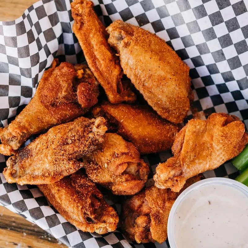 A basket of crispy chicken wings with celery and creamy dipping sauce.