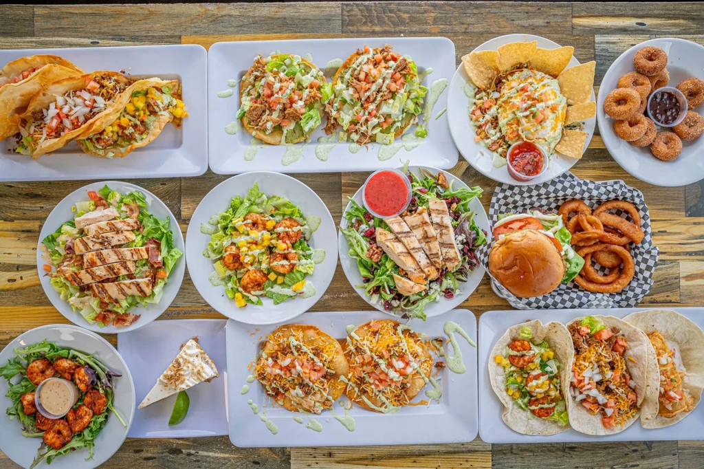 Overhead shot of a diverse restaurant food spread on a rustic table.