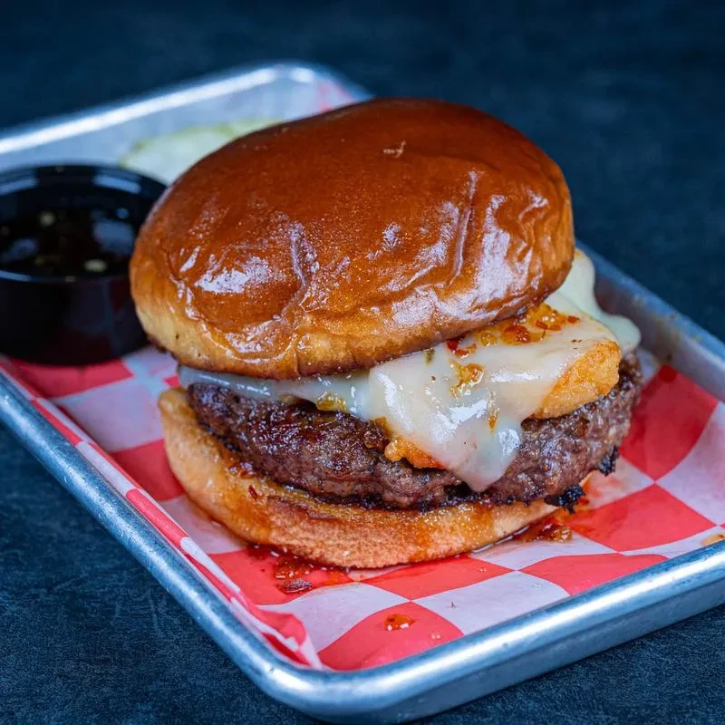 Top-down close-up: brioche burger with spiced melted cheese on tray.
