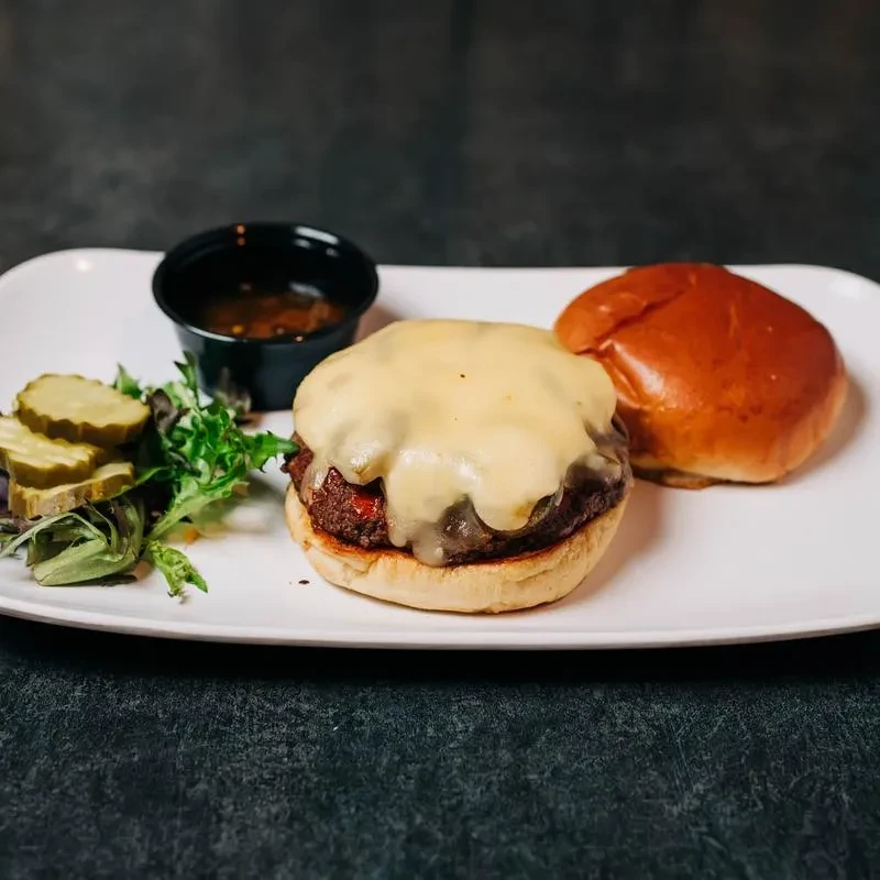 Open-faced burger, melted cheese, separate bun, pickles, greens, and sauce.