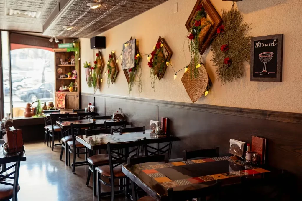 Warm restaurant dining room, patterned ceiling, decorative wall, empty set tables.