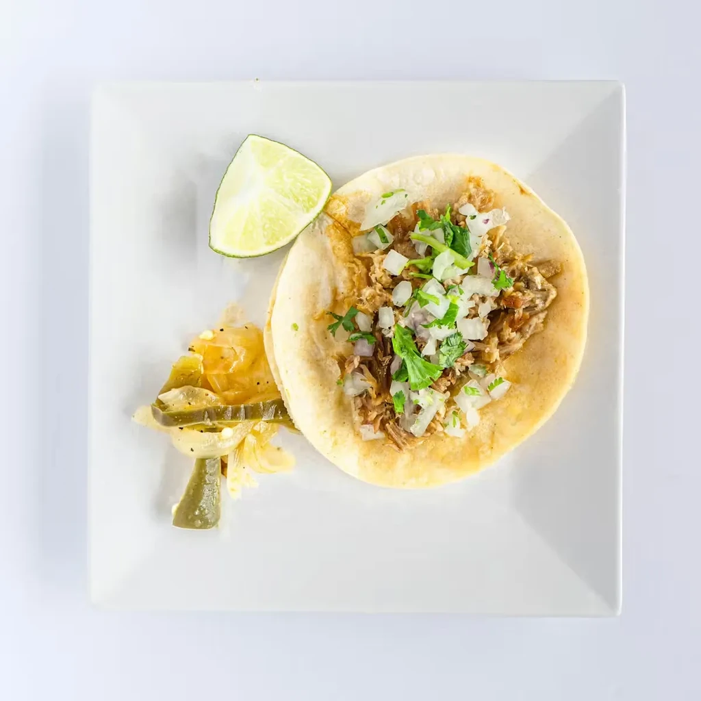 Taco with shredded meat, onions, cilantro, lime, and pickled jalapeños.