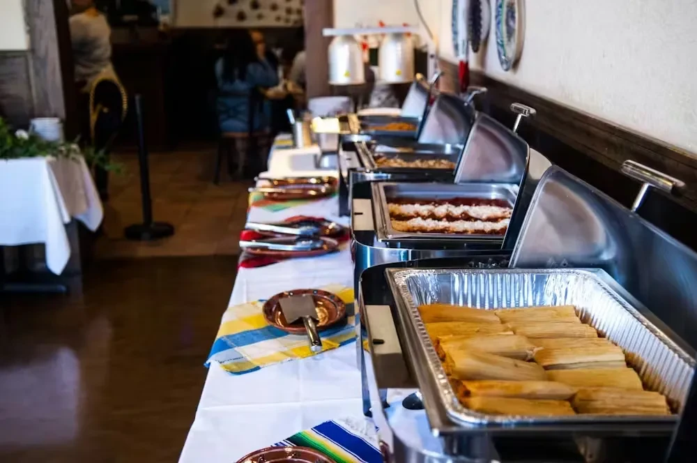 Buffet table features tamales, a casserole, and colorful Latin American placemats.