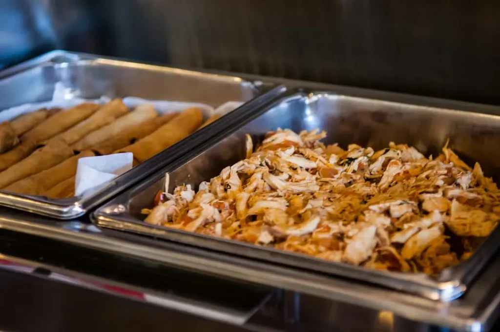 Two buffet warming trays with spring rolls and sauced pulled meat.