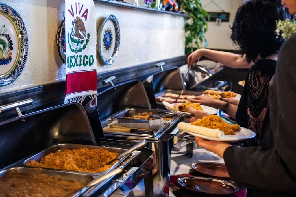 Vibrant Mexican buffet with rice, beans, and people serving food.