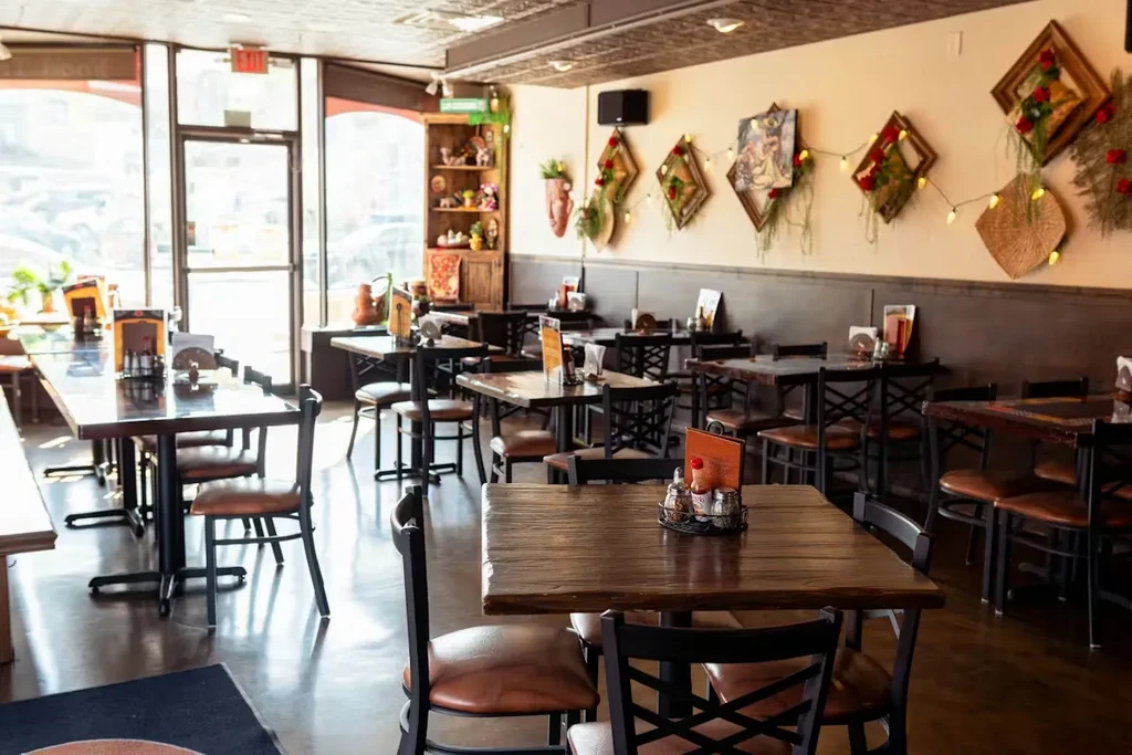 Empty restaurant dining area with dark tables, decorated walls, natural light.