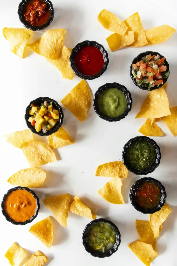 Overhead view: Nine colorful dips and salsas with tortilla chips.