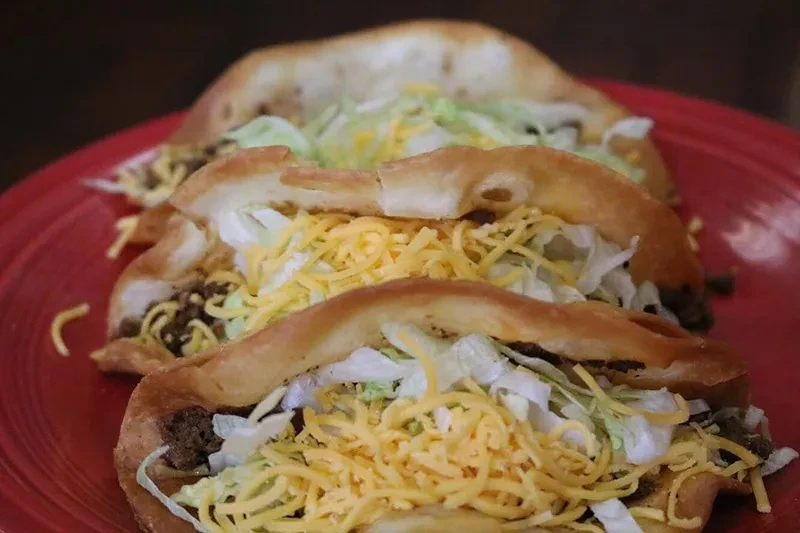 Three deep-fried tacos with meat, lettuce, and cheese on a red plate.