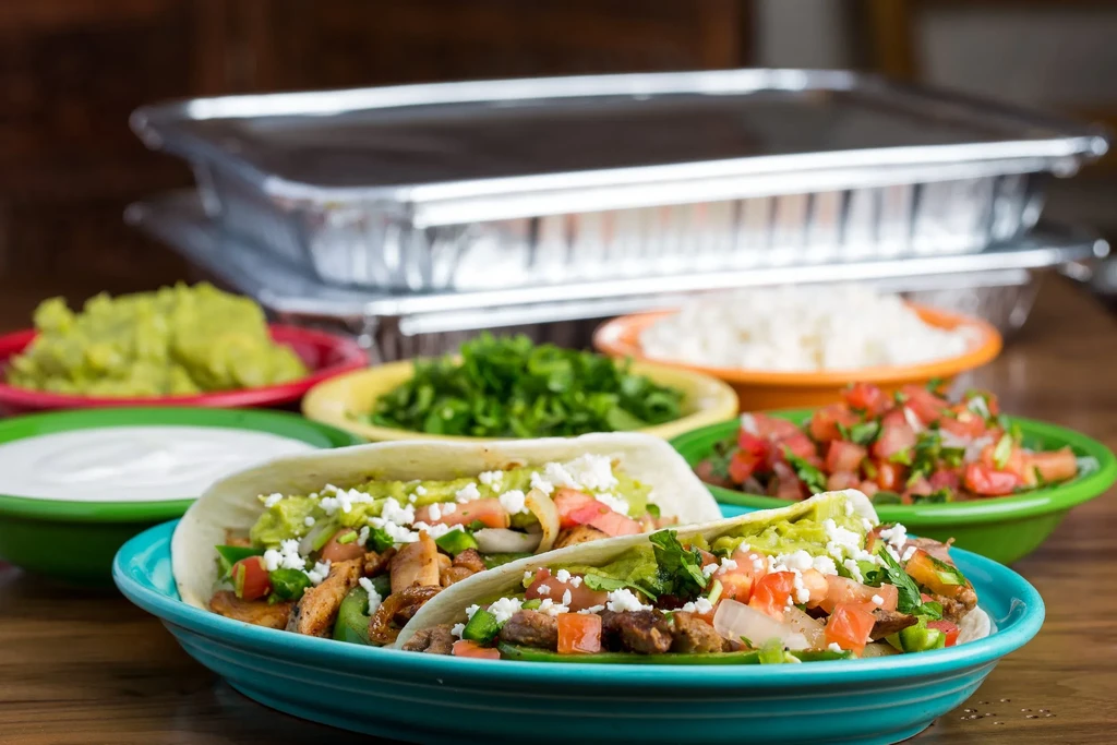 Close-up of grilled meat tacos, sides, and catering trays.