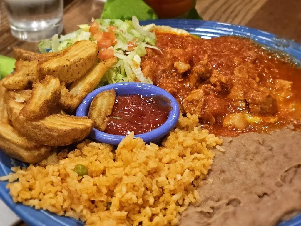 Blue plate of Mexican stew, potato wedges, rice, and refried beans.