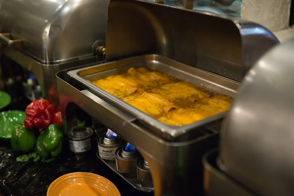 Cheesy enchiladas in a heated chafing dish at a buffet with peppers.