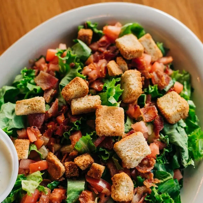 Close-up of fresh salad with lettuce, tomato, bacon, and croutons.