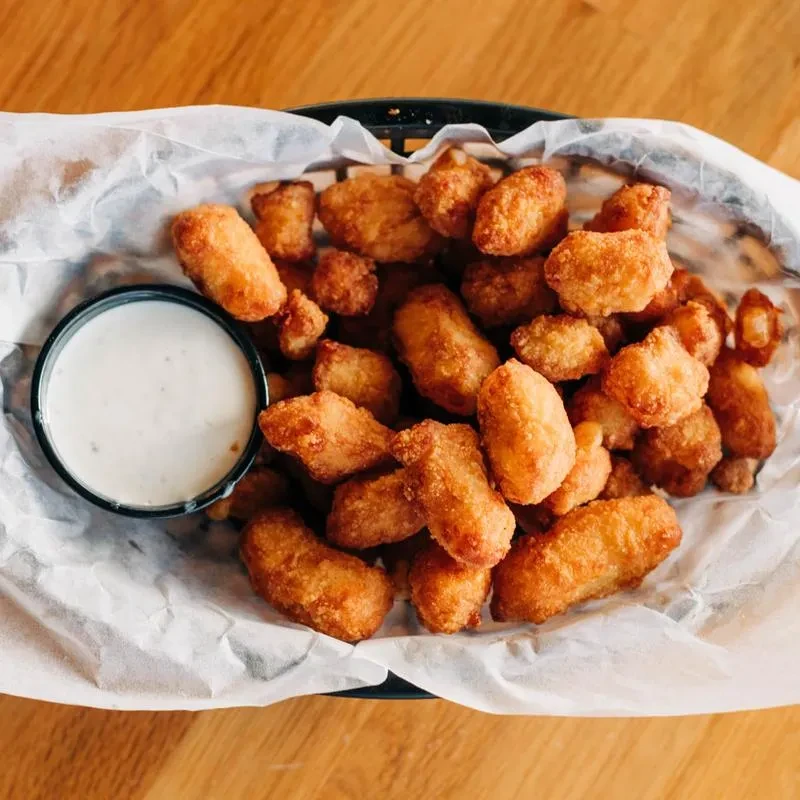 Golden-brown fried snacks in a basket with creamy dipping sauce.