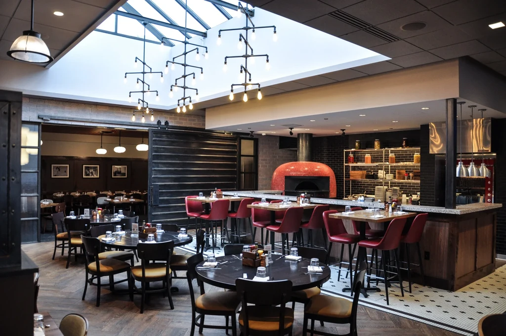 Contemporary restaurant interior featuring open kitchen, red pizza oven, exposed brick.