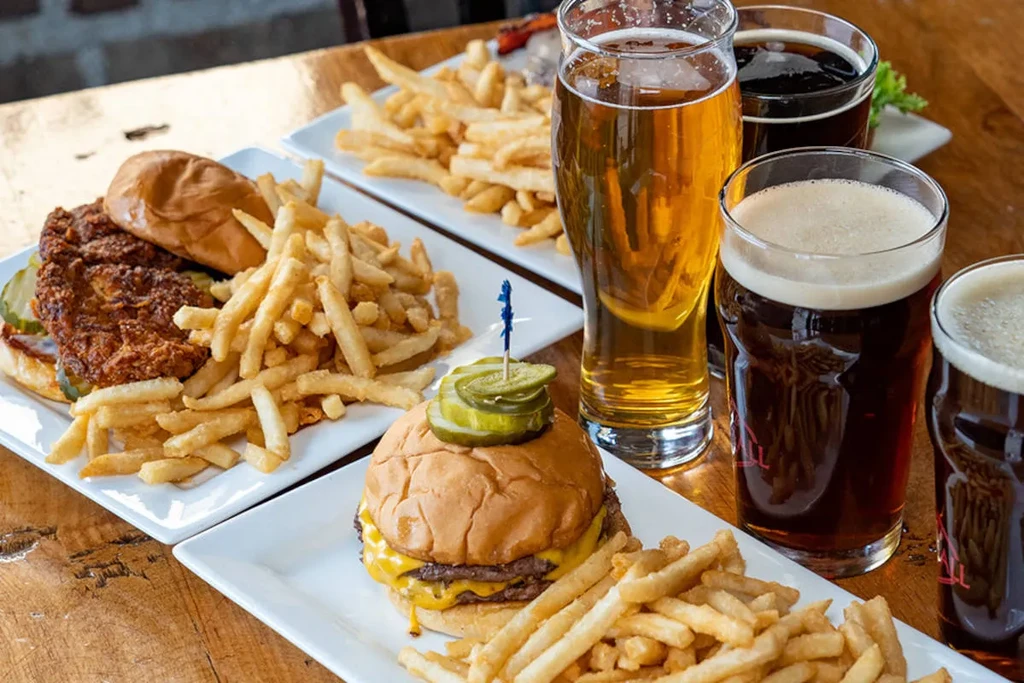 Fried chicken sandwich, cheeseburger, fries, and four beers on a wooden table.