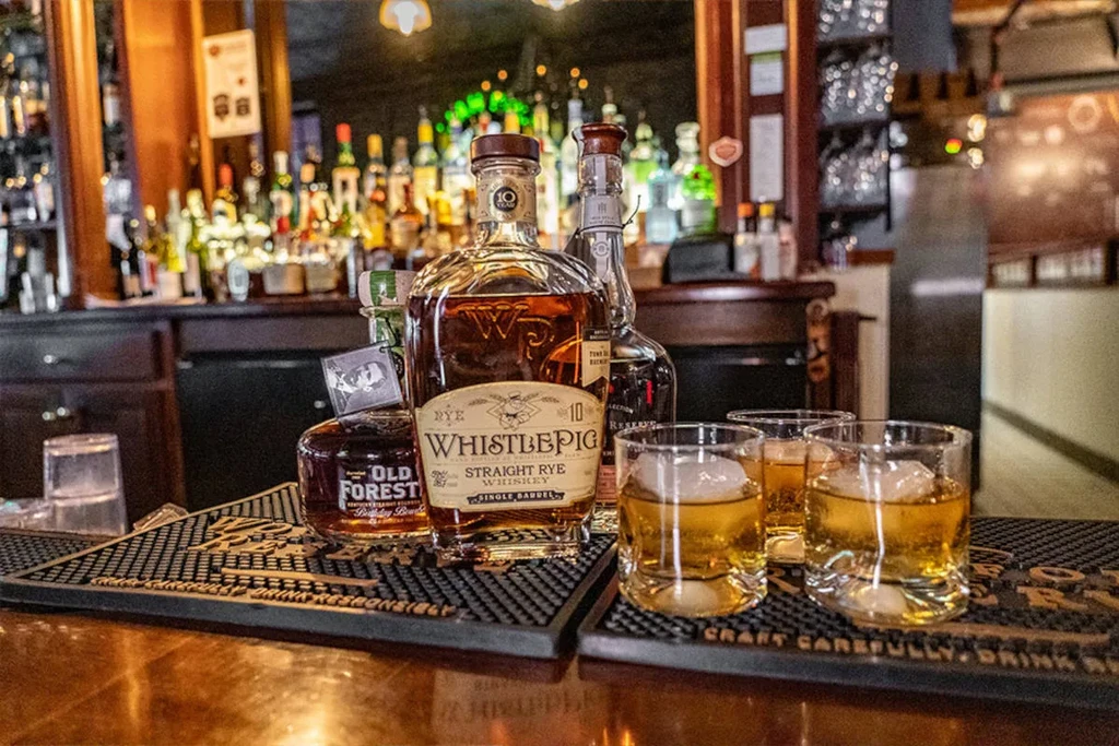 Whiskey bottles and three glasses with ice on black bar mats.