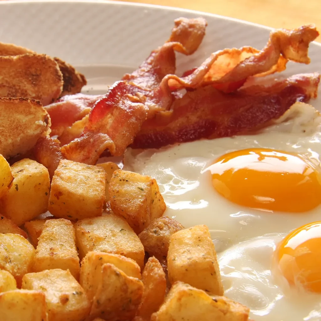 Breakfast plate with two sunny-side-up eggs, crispy bacon, home fries.