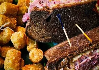 Two pastrami sandwiches with slaw and crispy tater tots.