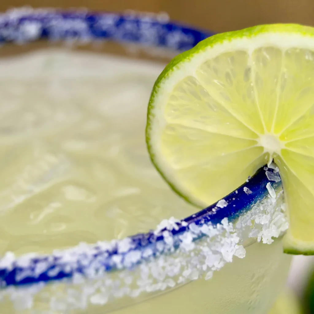 Vibrant margarita with lime wedge, blue patterned rim, and coarse salt.