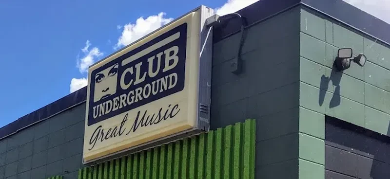 Illuminated 'CLUB UNDERGROUND Great Music' sign on a green paneled building.