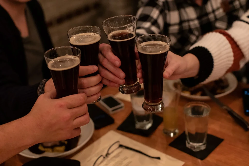 Four hands clink tall glasses of dark beer.
