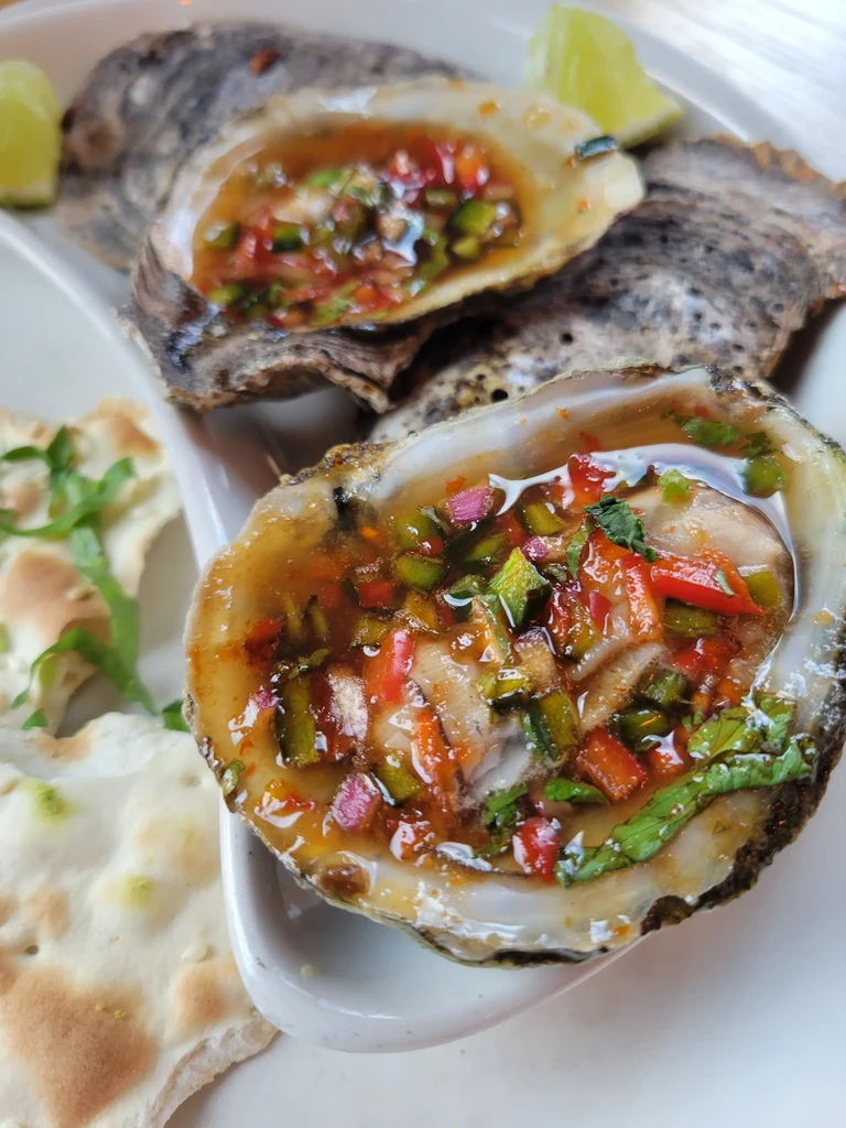 Oysters in shells topped with colorful diced peppers and herbs.