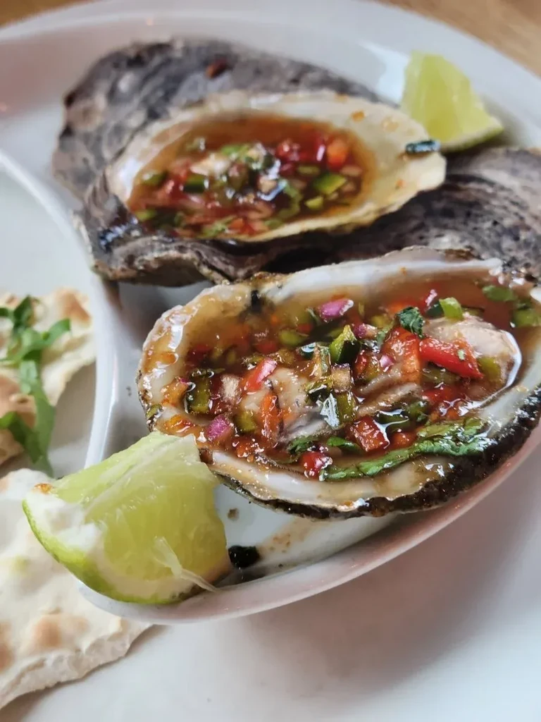Two oysters in shells with colorful salsa and lime on a plate.