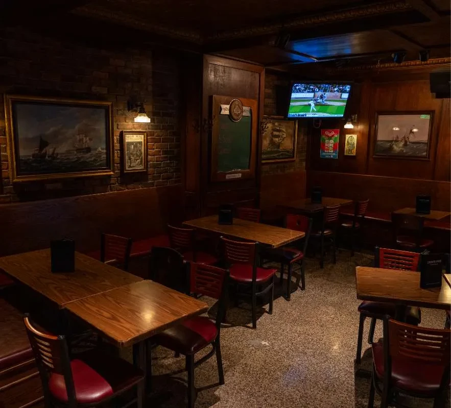 Rustic restaurant interior with dark wood, ship paintings, and a TV.
