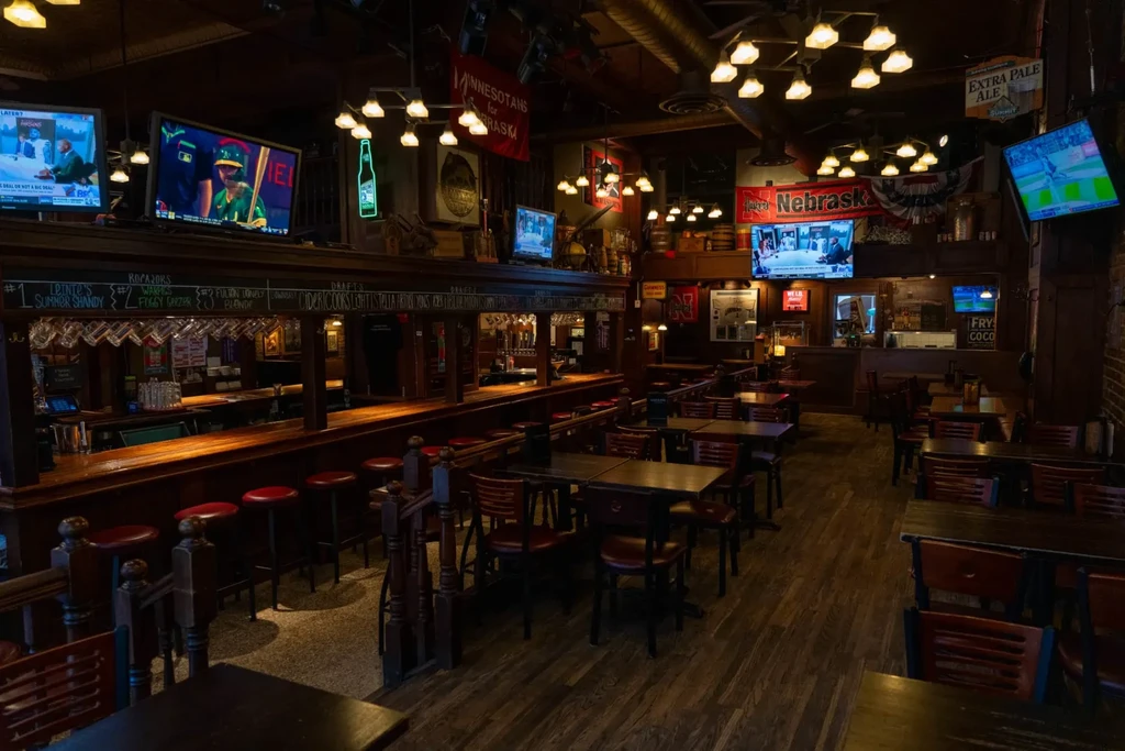 Empty, dimly lit rustic sports bar interior with wooden bar and tables.