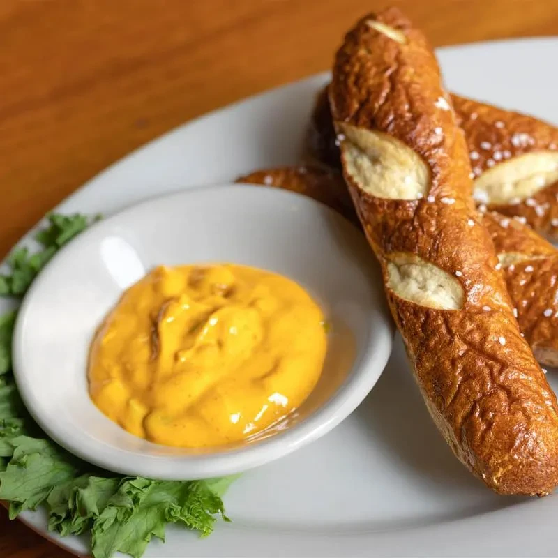 Golden pretzel sticks, yellow dipping sauce, and lettuce on a white plate.