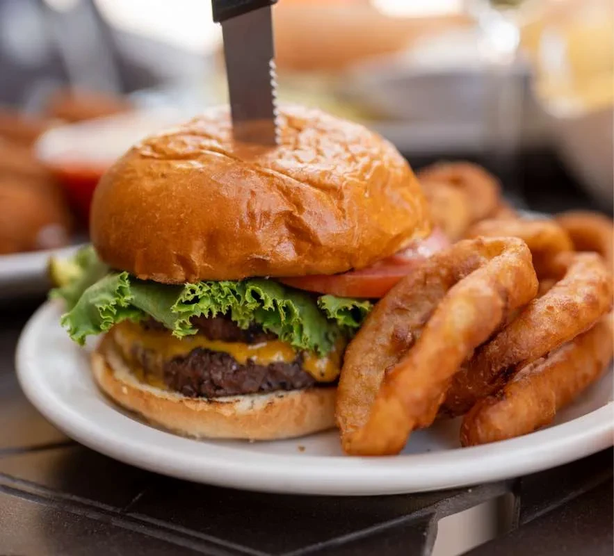 Double cheeseburger, onion rings, and knife on a white plate.