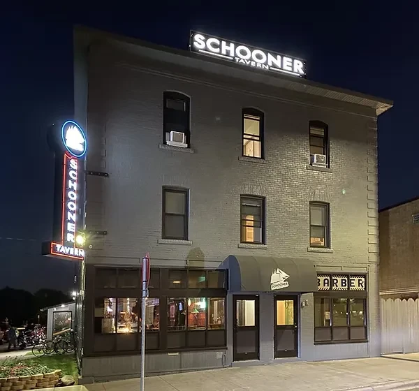Nighttime view of a three-story brick Schooner Tavern with neon signs.